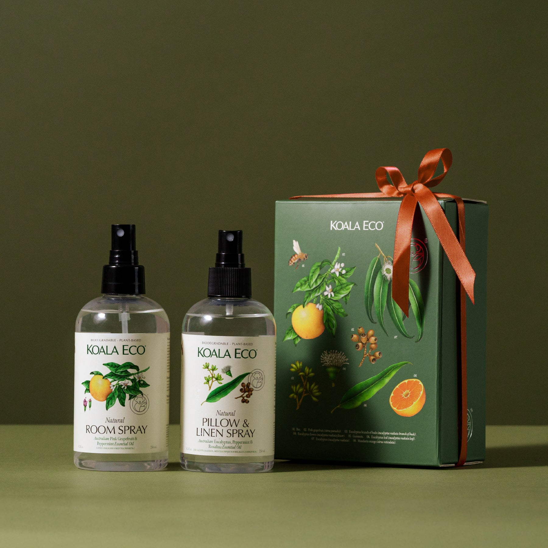 Two bottles from the "Aromatherapy Gift Collection - Room & Linen" set by Koala Eco are placed beside a coordinating ribbon-wrapped box, all against a green backdrop.