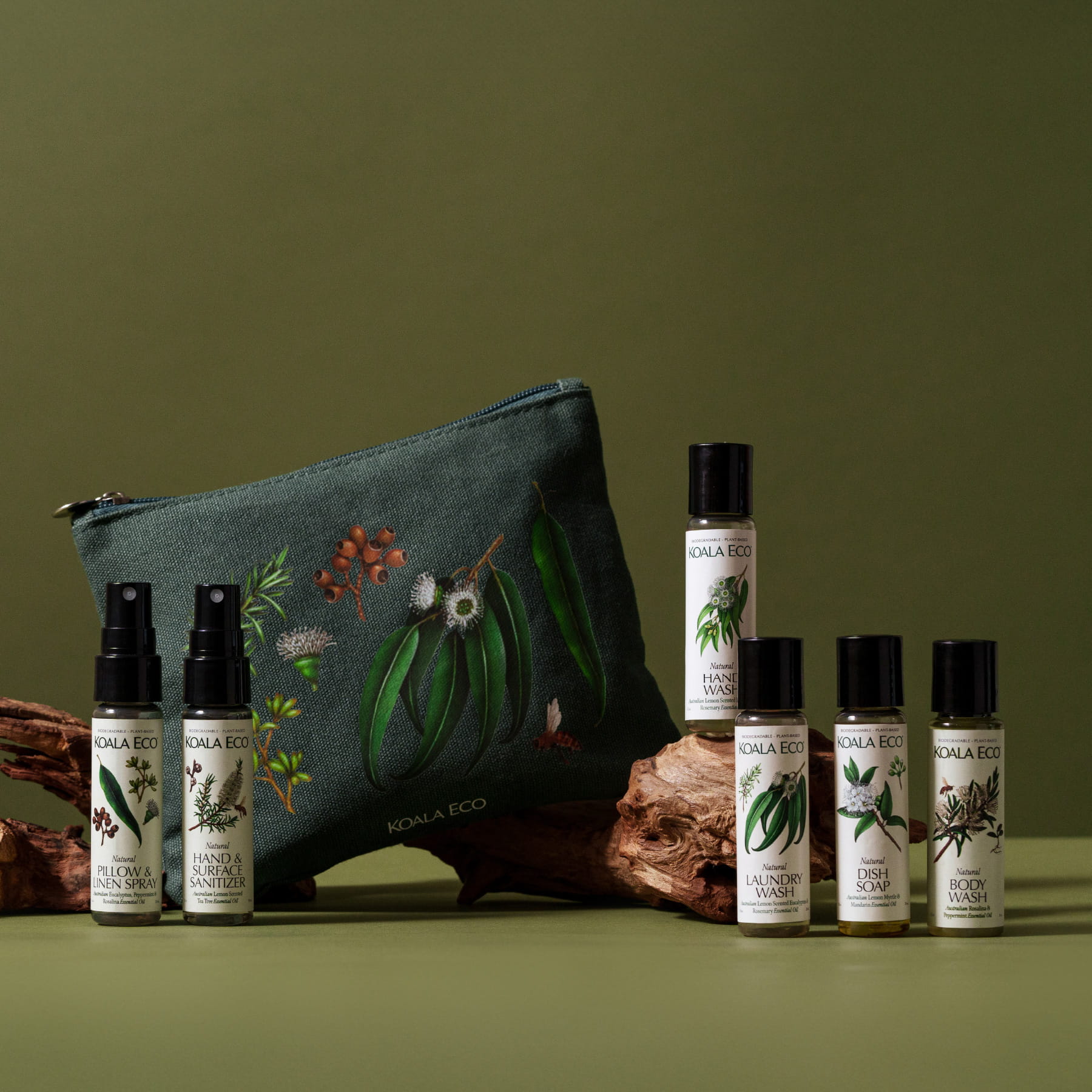 The Essentials Kit from Koala Eco, featuring a green pouch adorned with botanical illustrations, are six small bottles of Koala Eco products with green background.